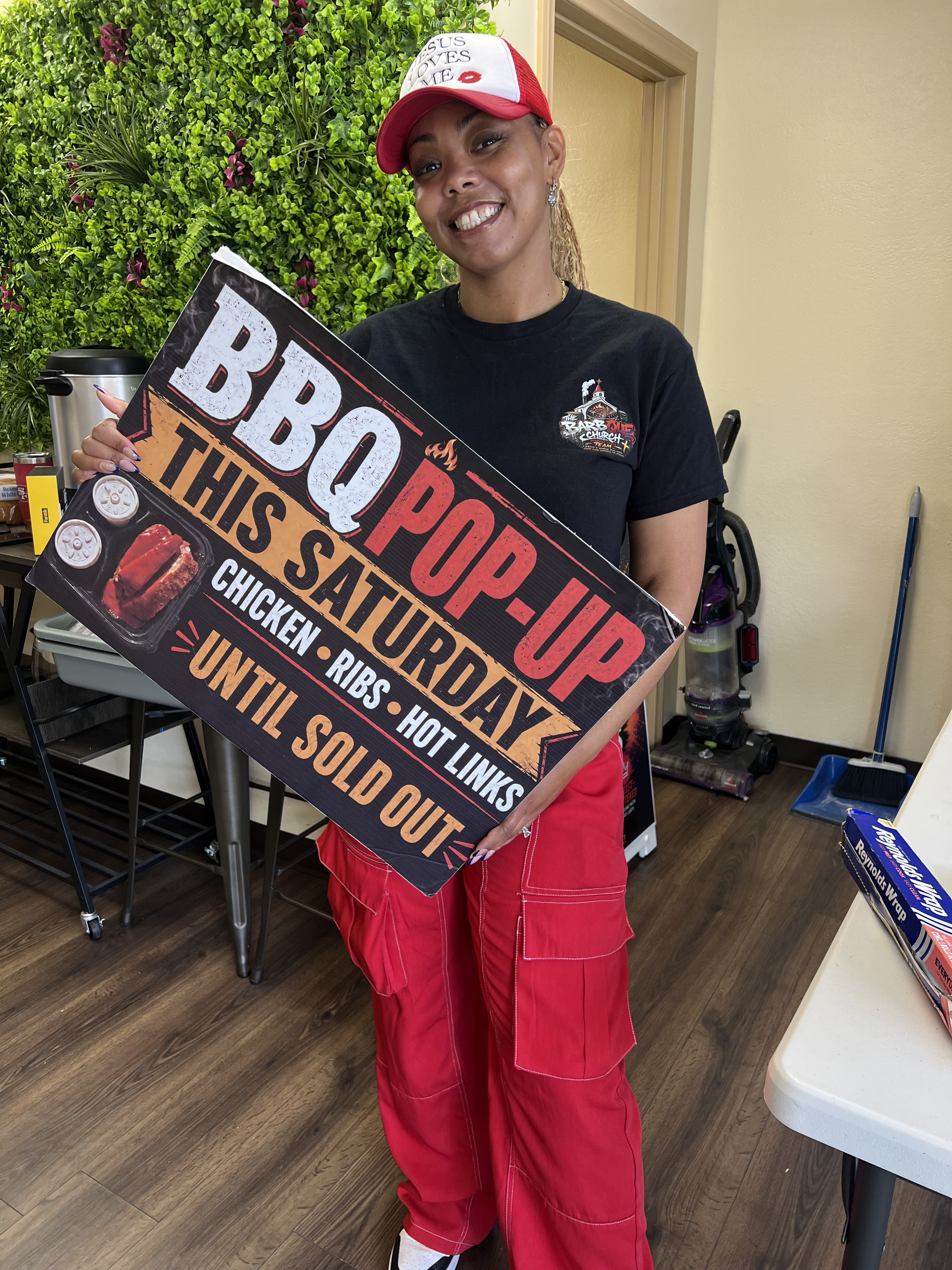 BBQ Church team member holding a Saturday pop-up sign for chicken, ribs, and hot links