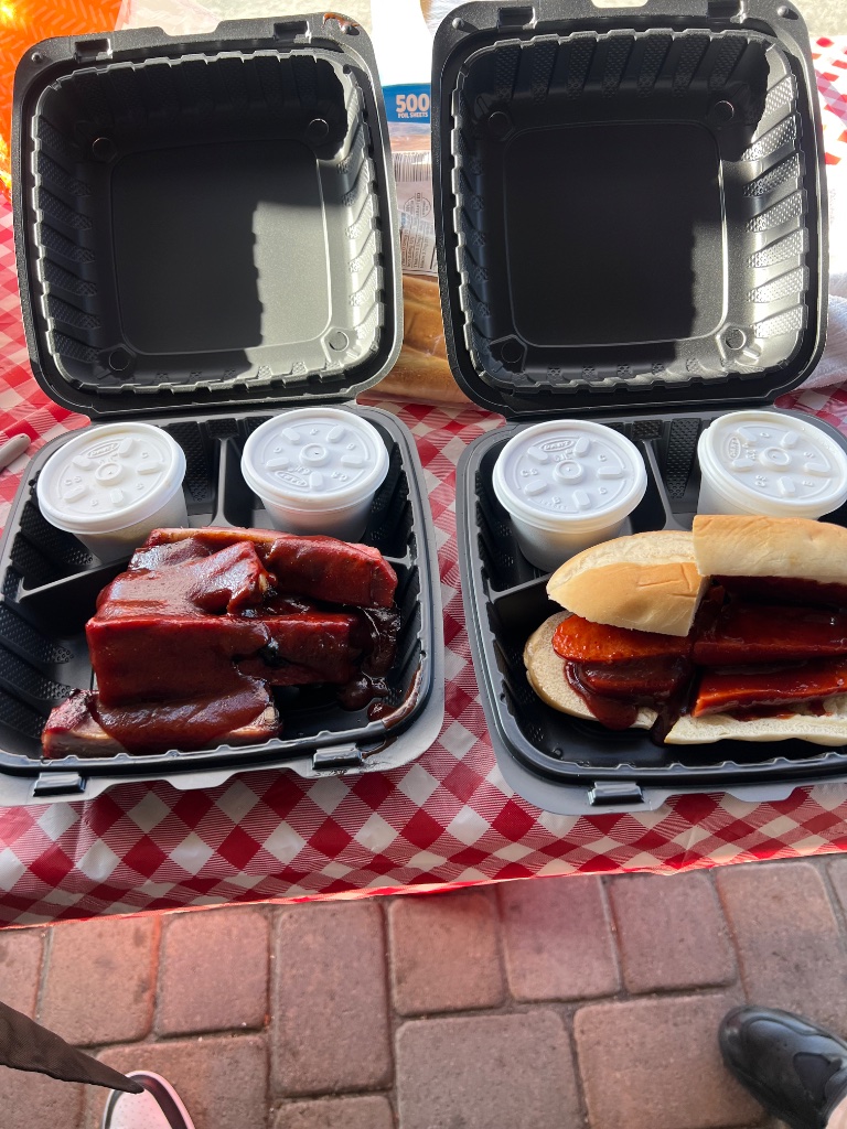 Two BBQ takeout containers with ribs and a sandwich