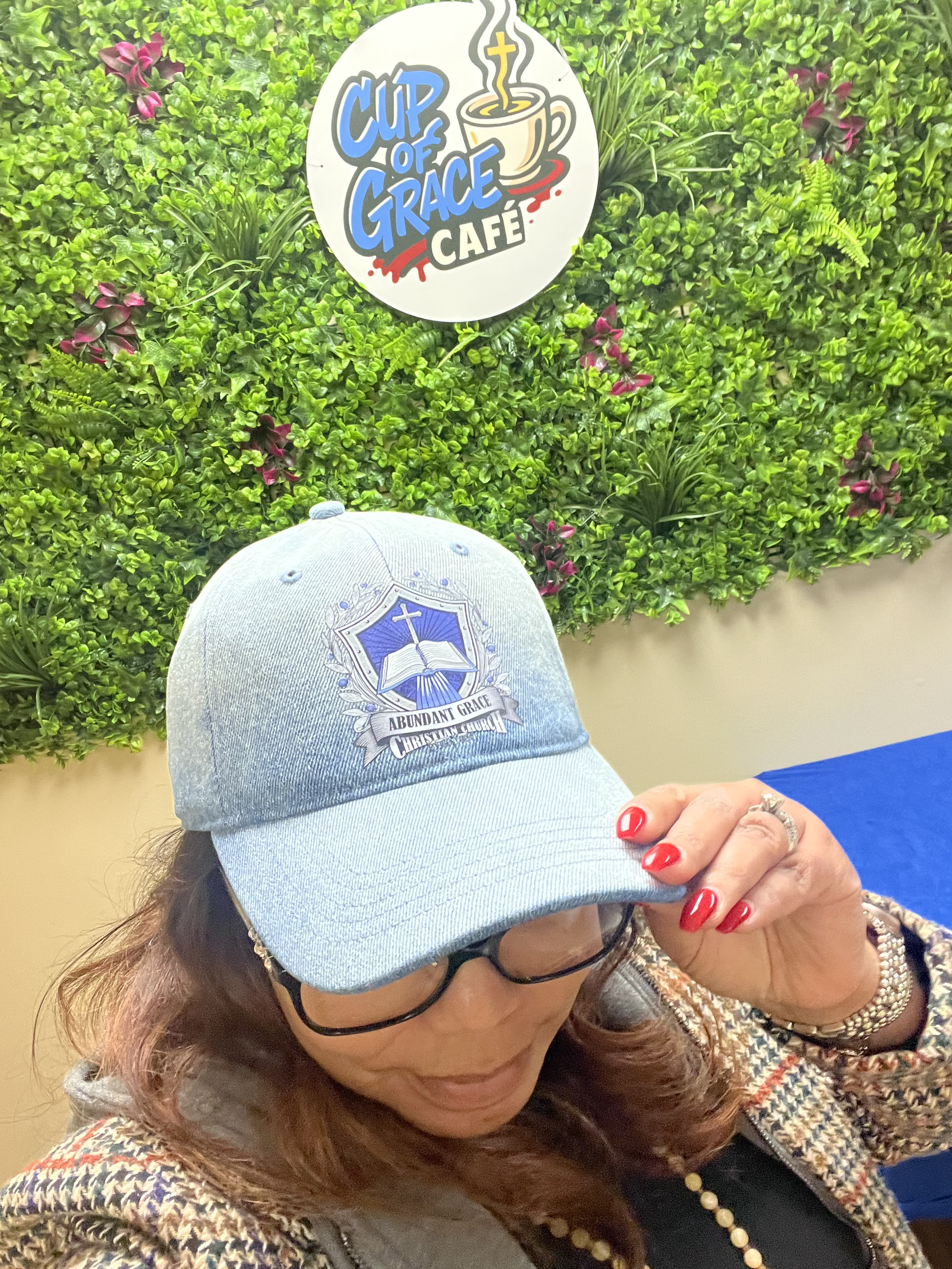 A member wearing an Abundant Grace cap in front of the café green wall