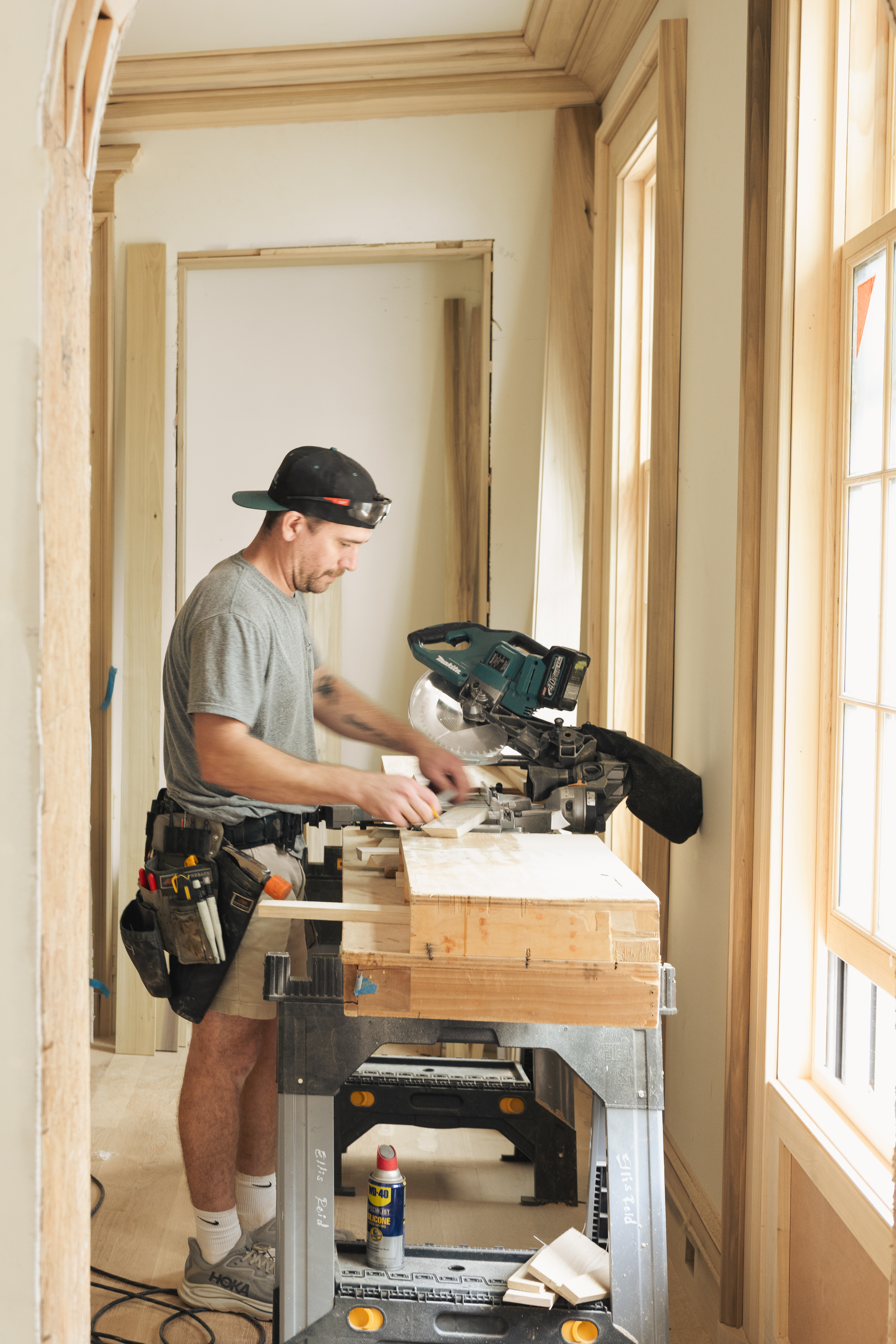 Ellis-Reid carpenter cutting trim at a miter saw inside a finished home