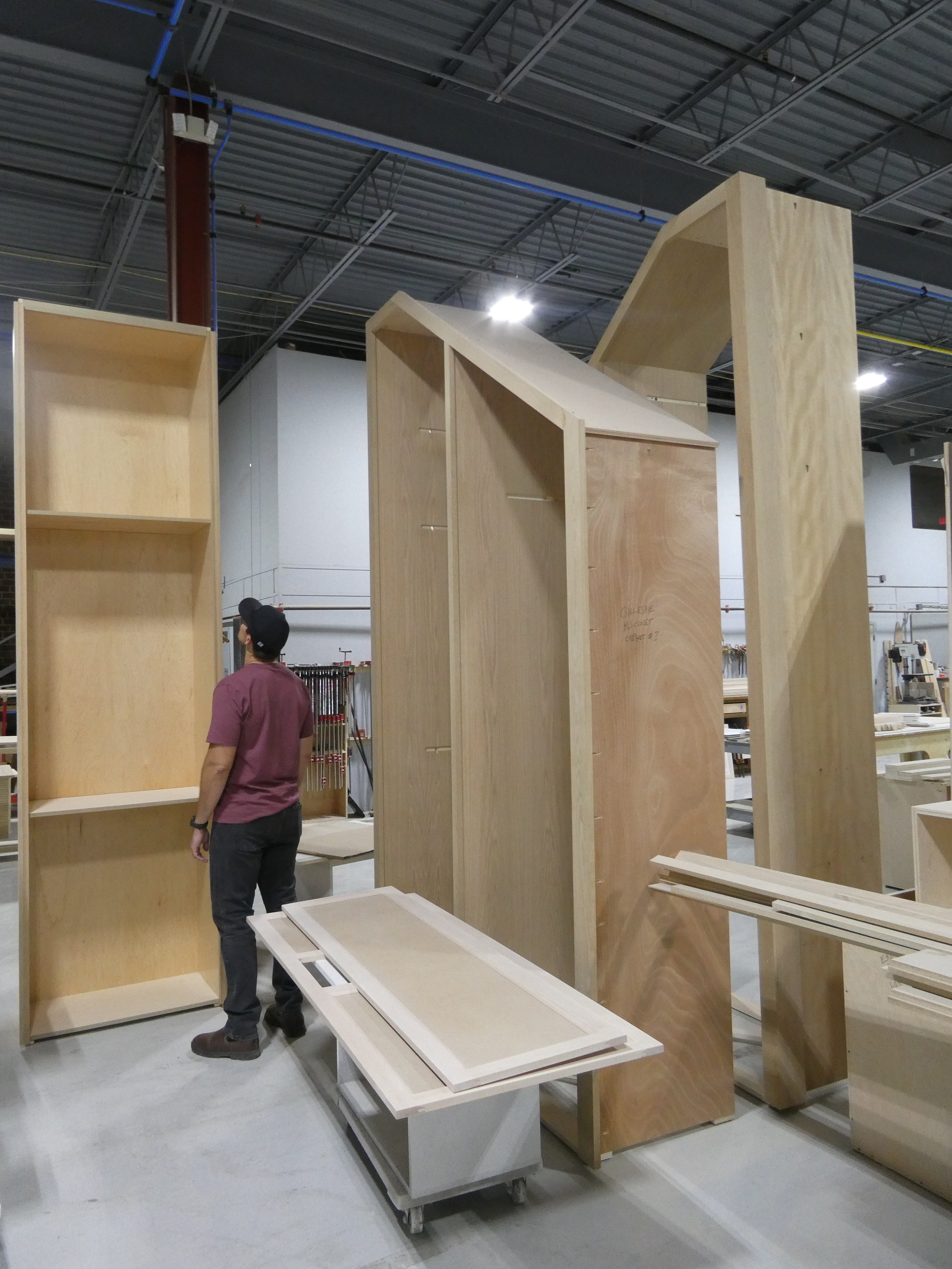 Tall cabinet cases and a door dry-fit standing on the shop floor beside a craftsman.
