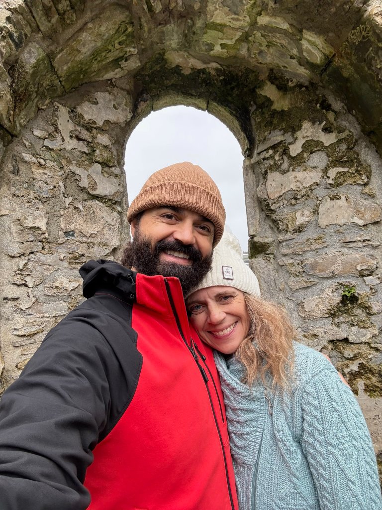 BJ and Val beneath an ancient stone archway — a life of heritage preservation, spiritual practice, and intentional community.