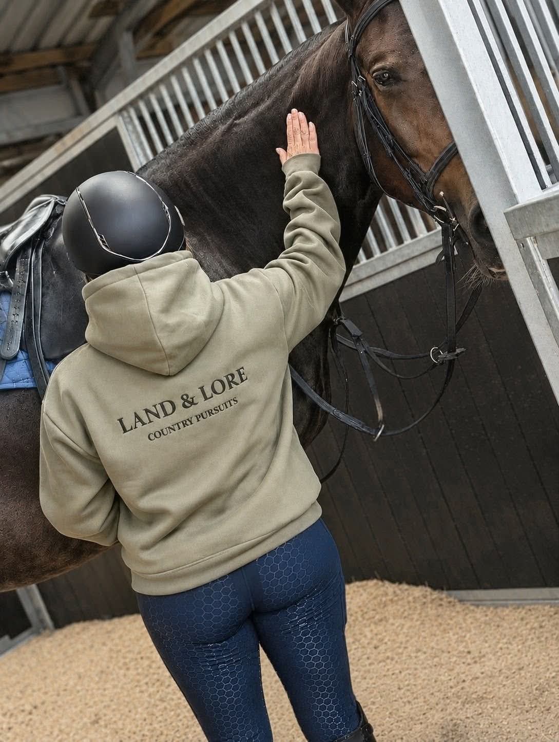 Person in sage Land & Lore hoodie with a horse in the stable