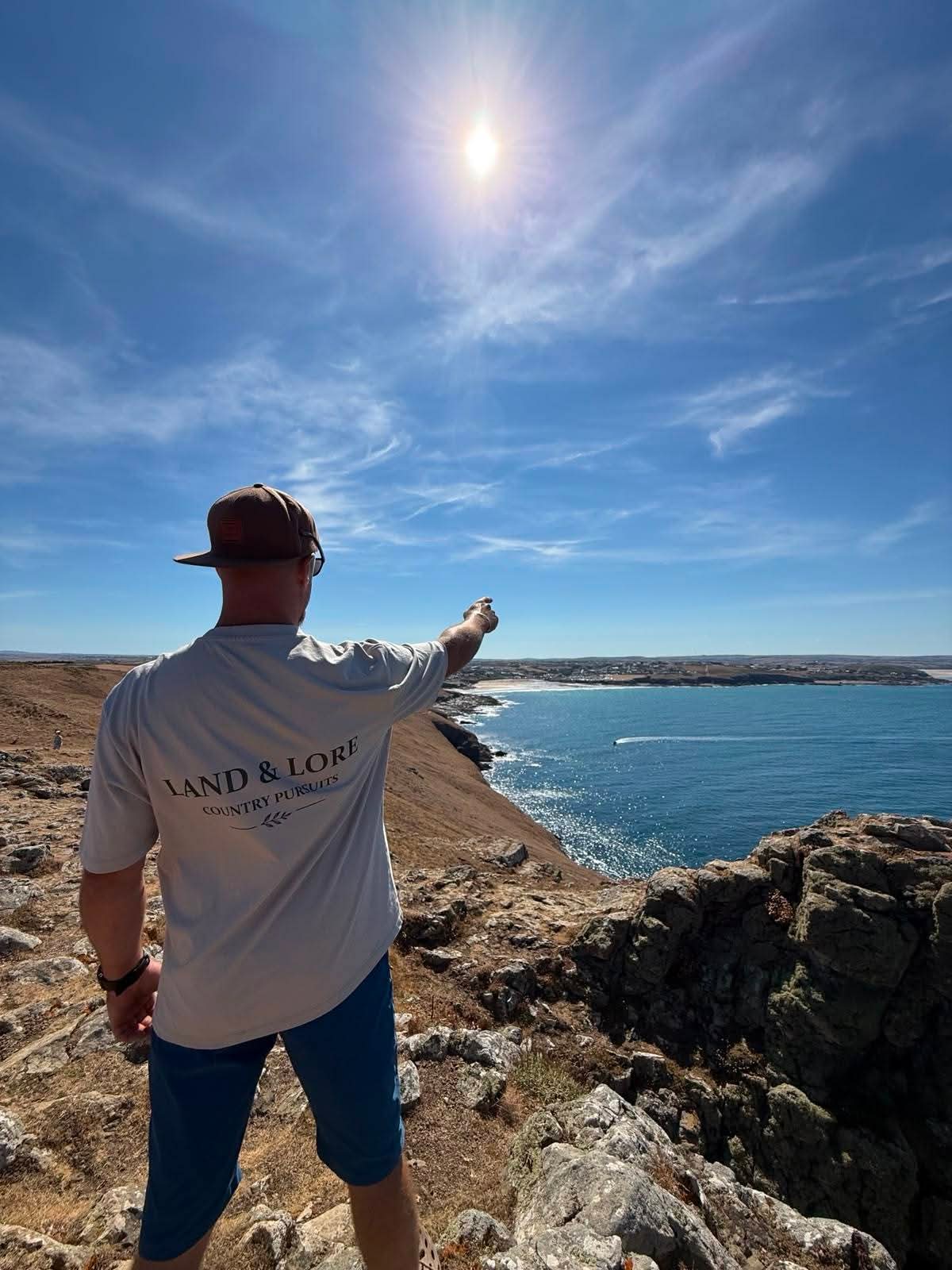 Person in stone Land & Lore t-shirt pointing toward the sea from a cliff