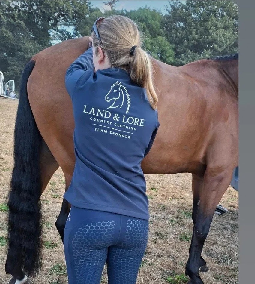 Team sponsor in navy Land & Lore top and leggings with a horse in the field