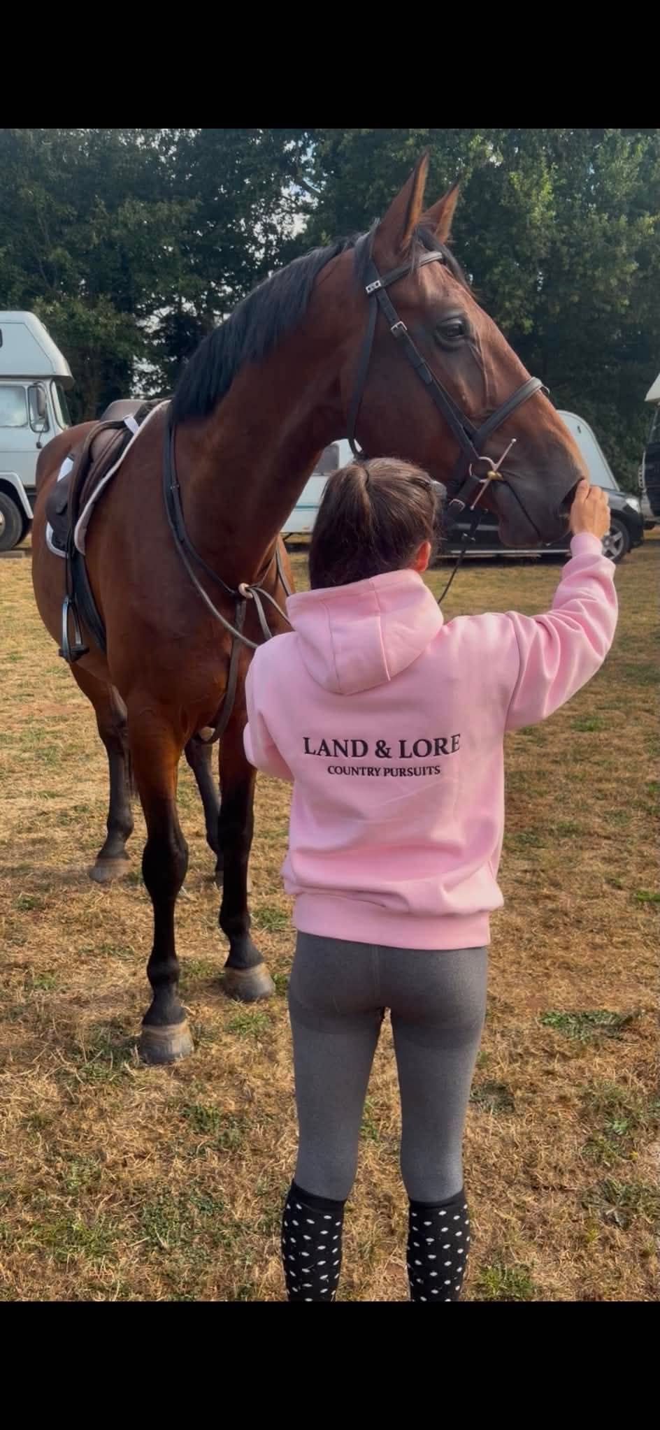 Person in pink Land & Lore hoodie touching a horse muzzle