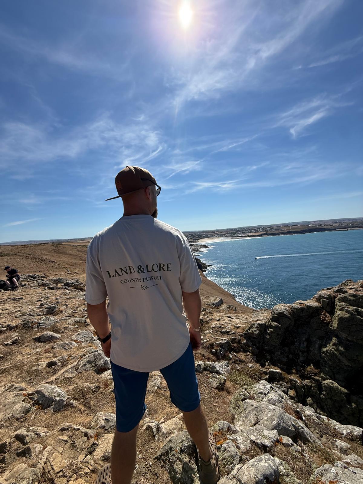 Man wearing Land & Lore t-shirt looking out over the sea from a cliff