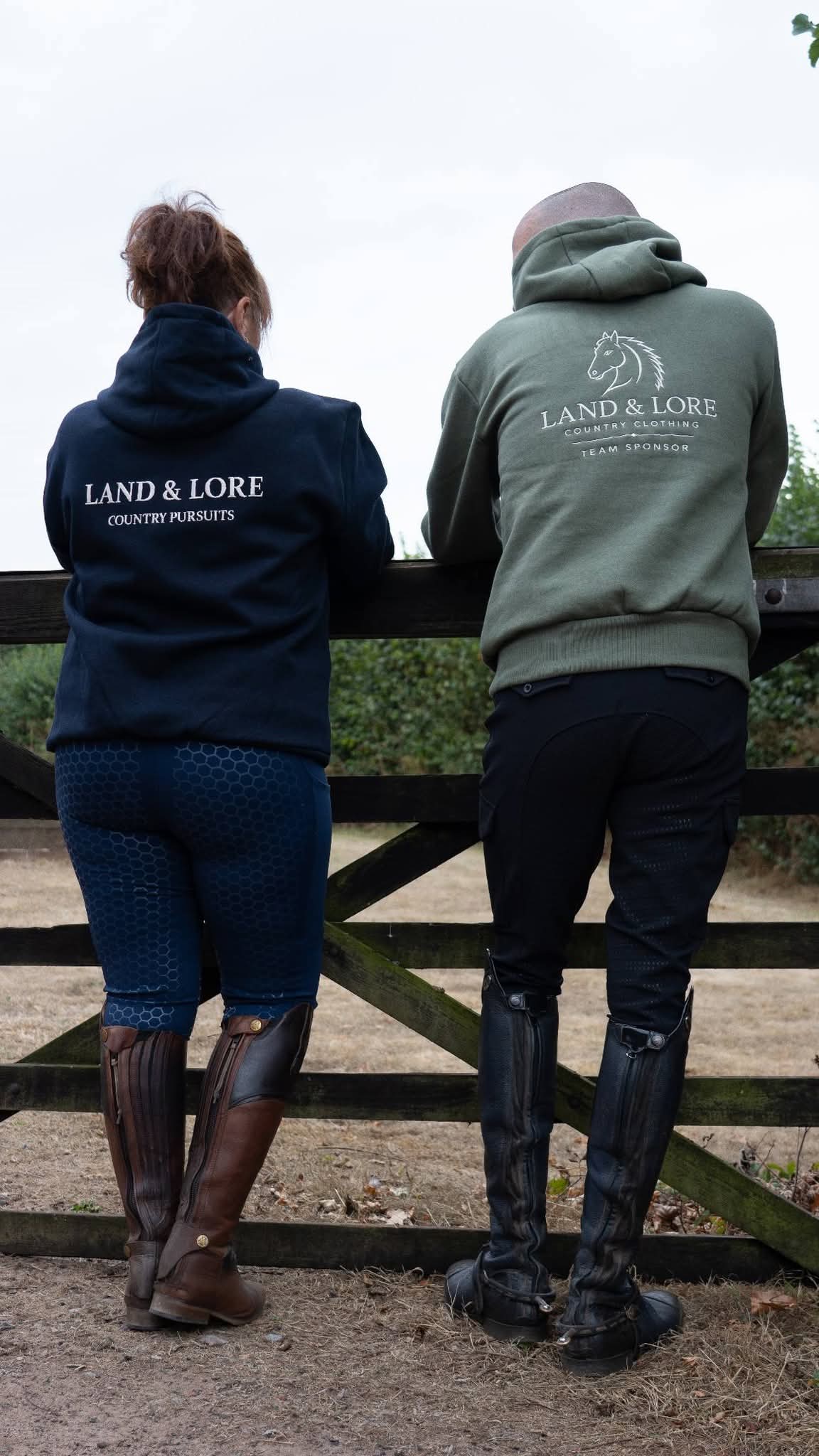 Two team sponsors in navy and olive Land & Lore hoodies by a fence