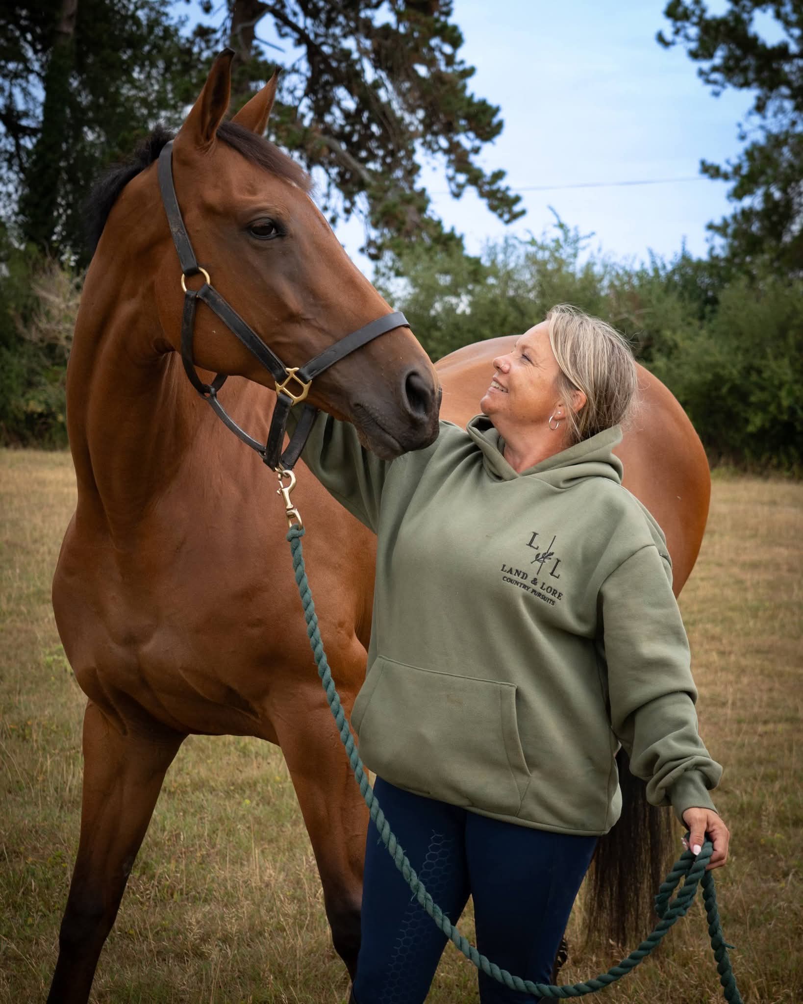 Woman in sage Land & Lore hoodie with a horse in the field