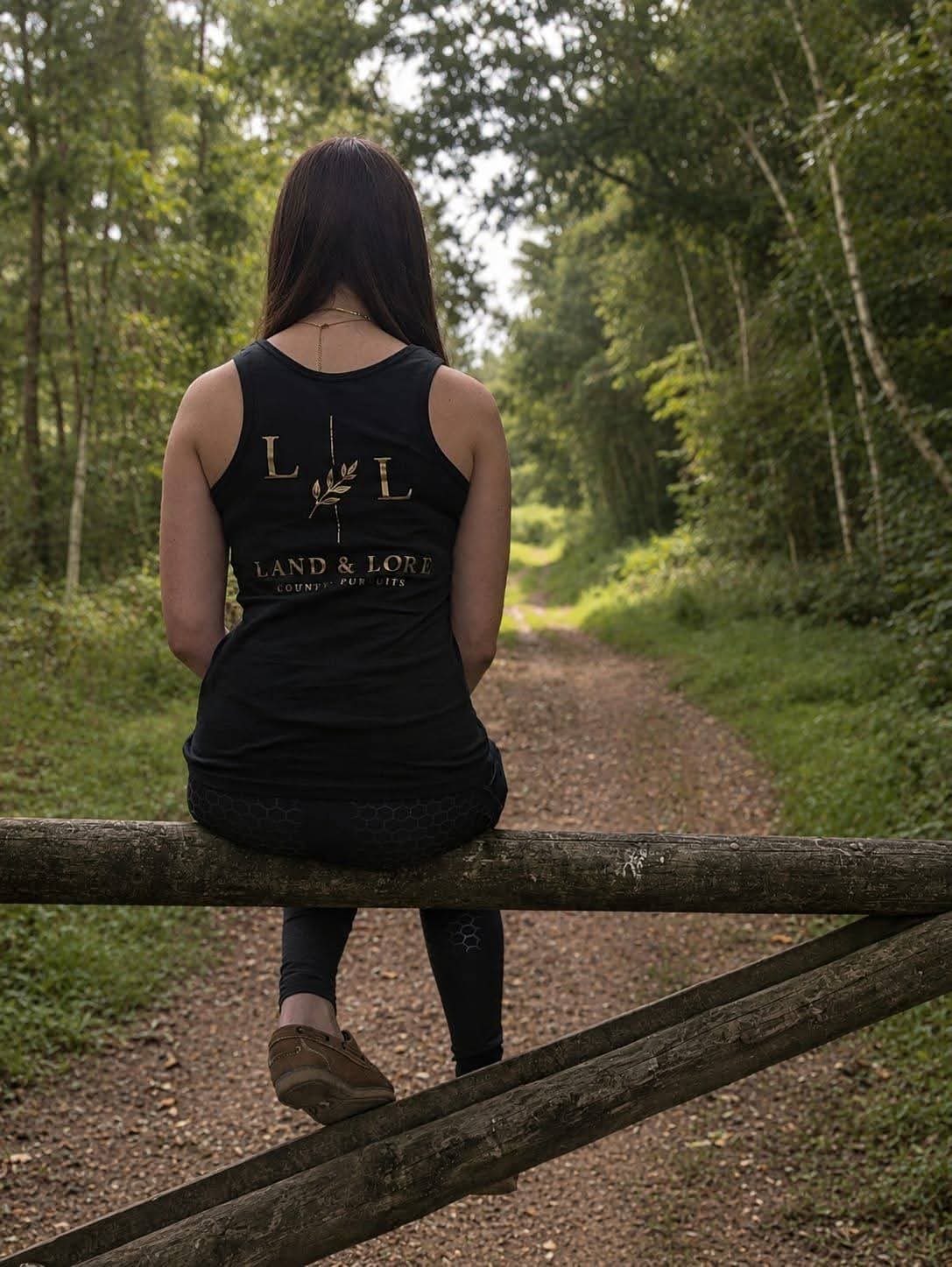 Woman in black Land & Lore tank top seated on a wooden fence