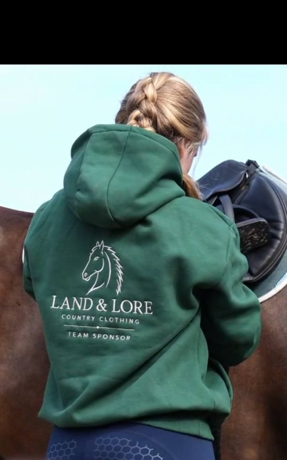 Team sponsor in green Land & Lore hoodie reaching for a horse