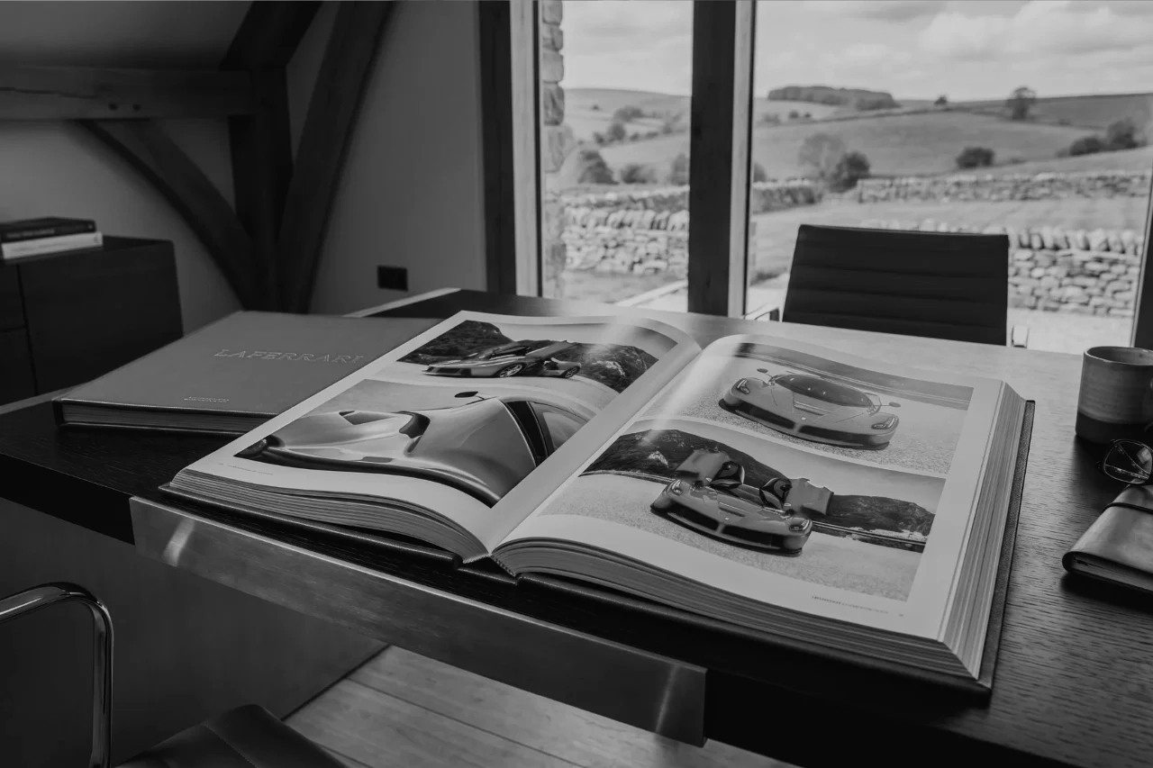 An open collector's book of LaFerrari photographs on a wooden desk