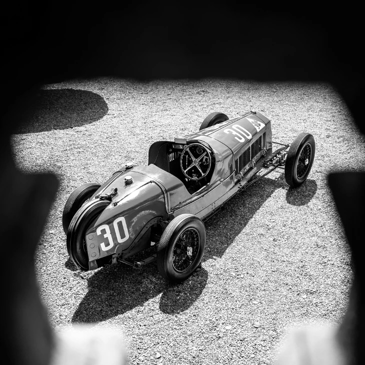 Vintage grand prix car framed by a dark archway, in black and white