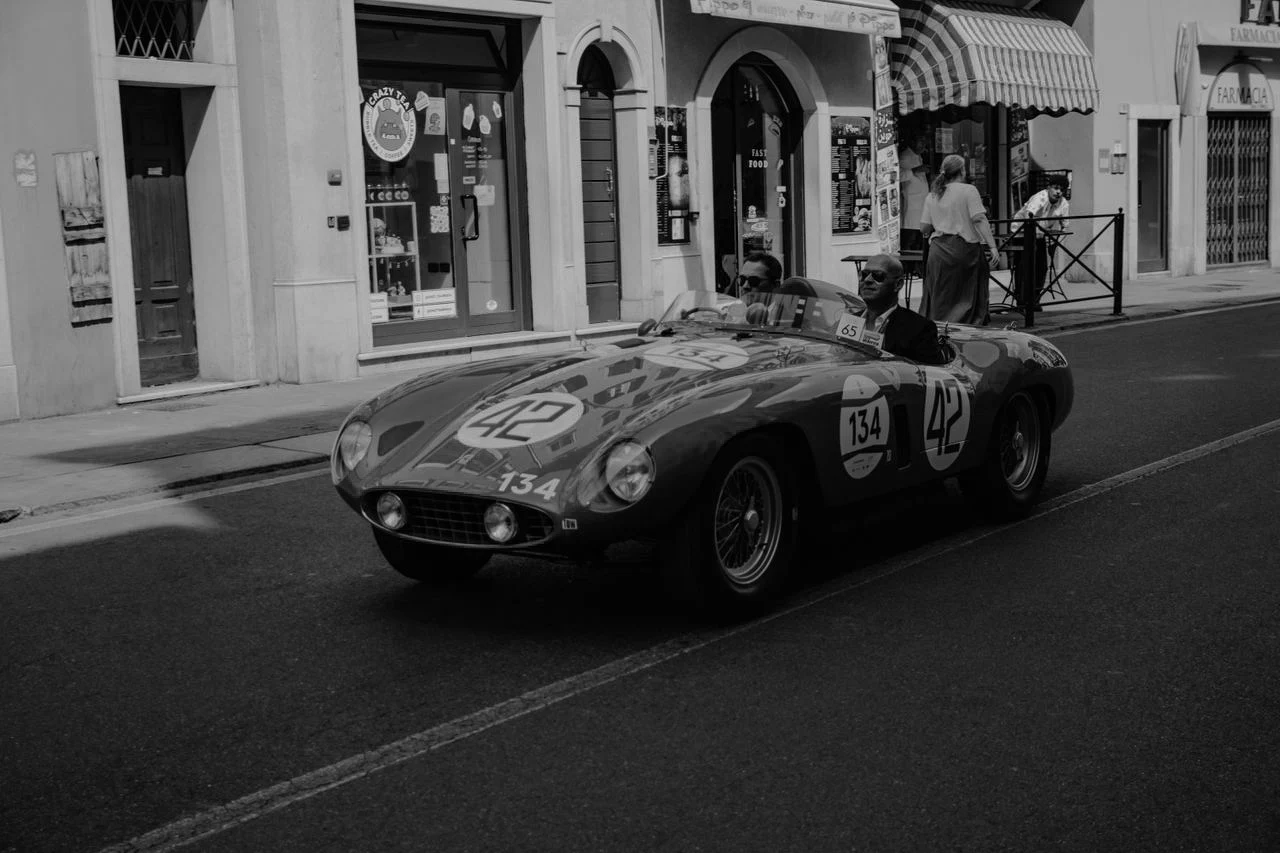 A vintage race car numbered 42 driving down a town street, black and white