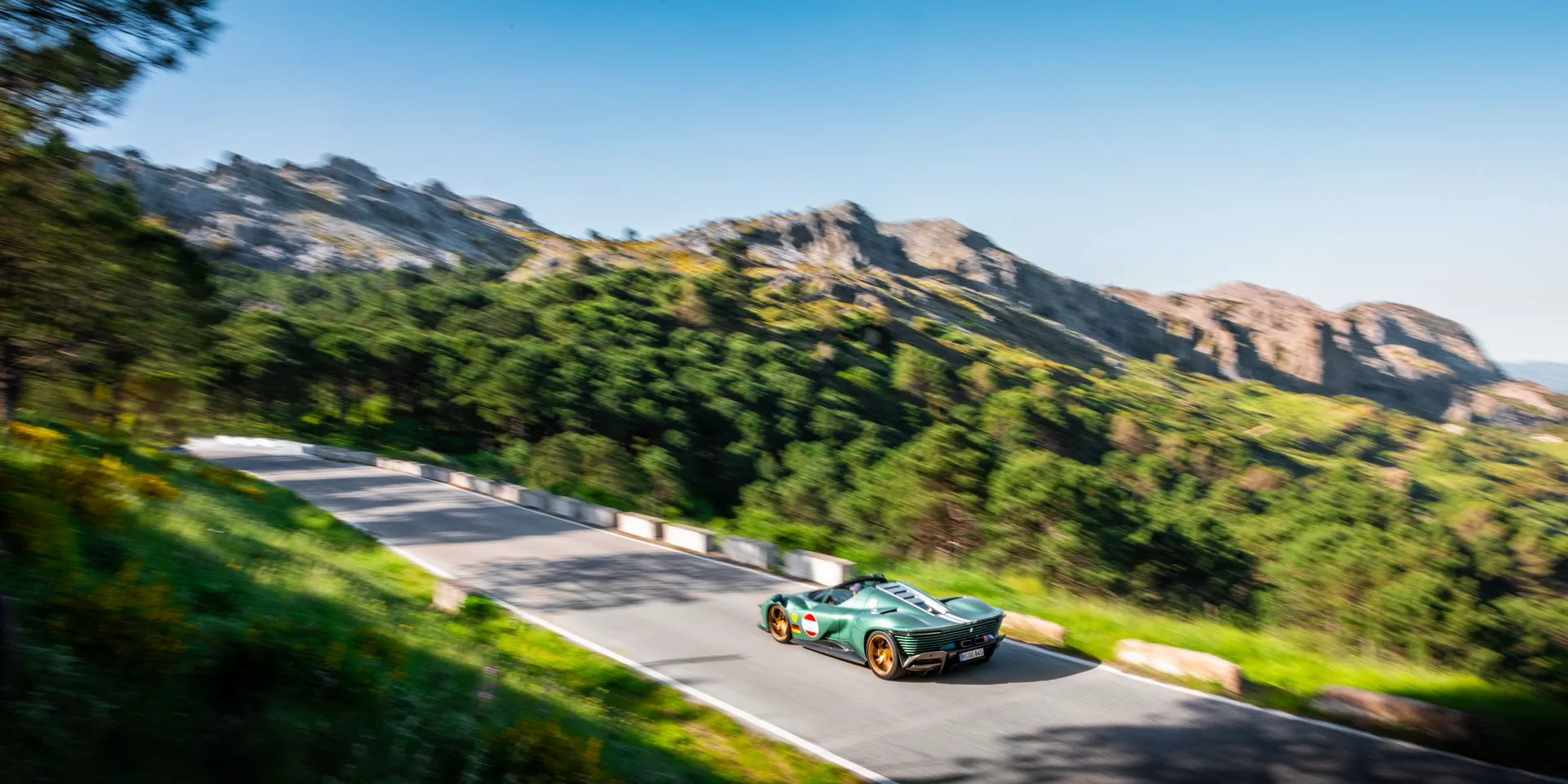 A green open-top sports car driving along a winding mountain road