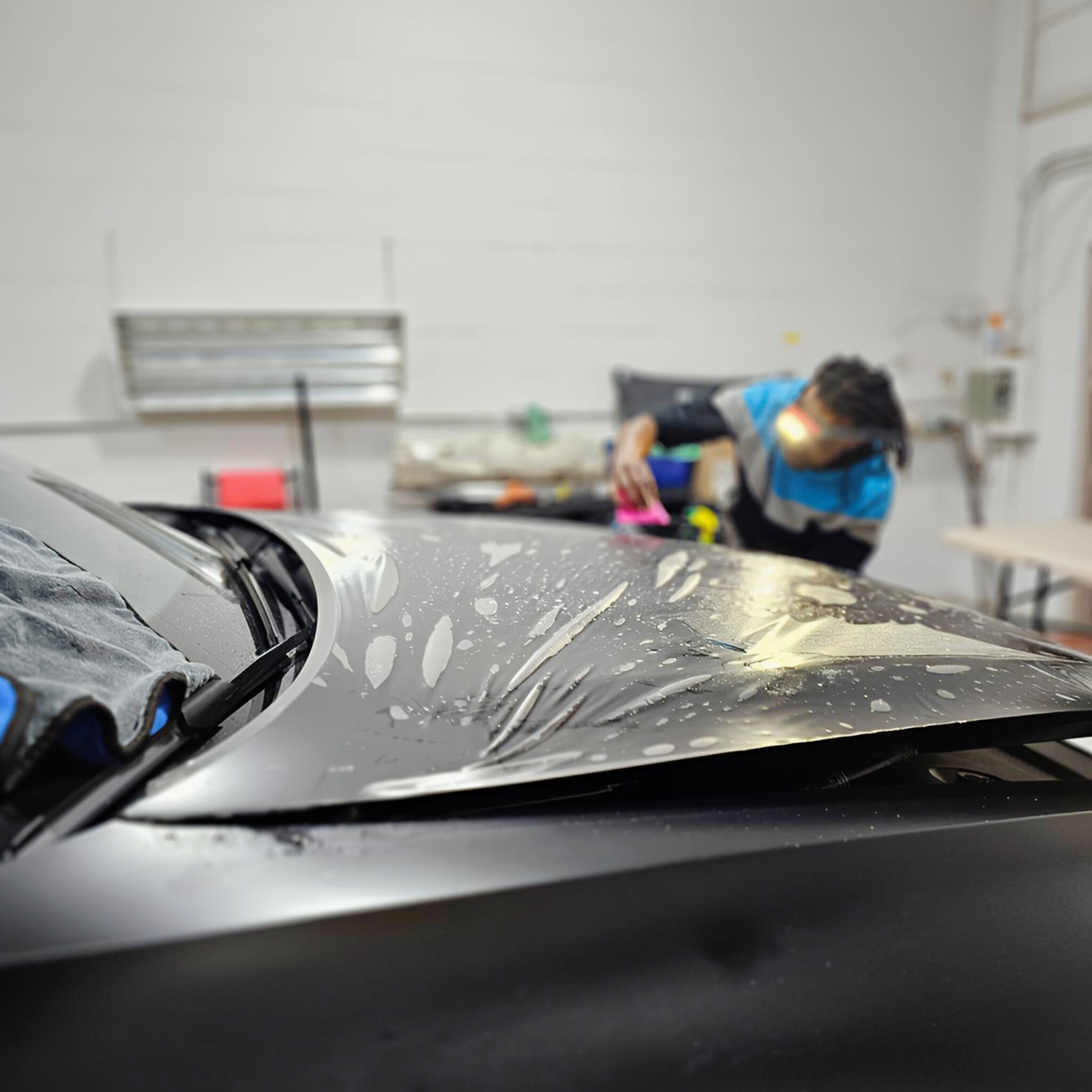 Technician with a headlamp working paint protection film flat on the hood with a squeegee