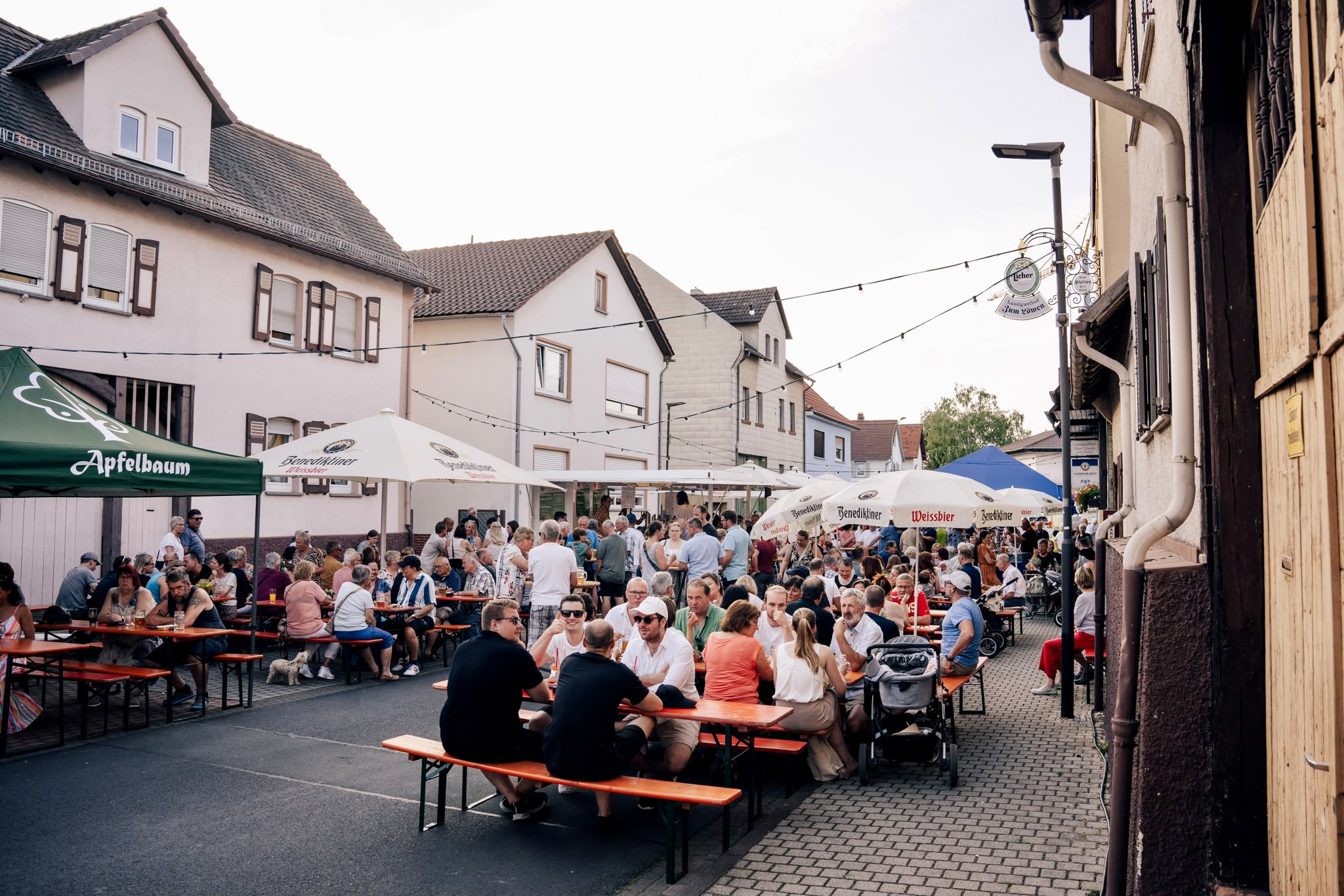 Straßenfest mit langen Tischen, Sonnenschirmen und Lichterketten