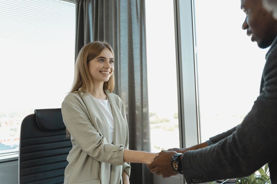 A new hire shaking hands with a colleague on their first day in a bright office.