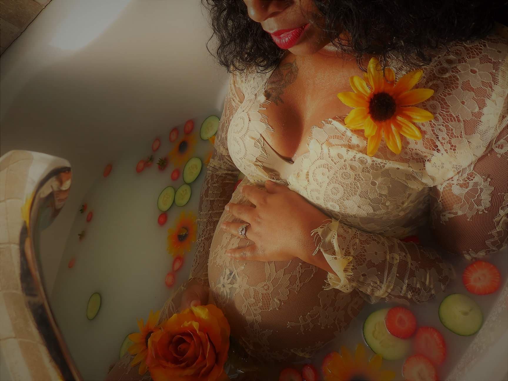 Expectant Black mother in a cream lace gown resting her hand on her belly in a floral milk bath — Atlanta's Baby Consultants doula support