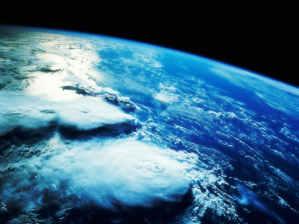 Earth from high orbit — a tropical cyclone over deep blue ocean, the glowing atmospheric limb against the black of space