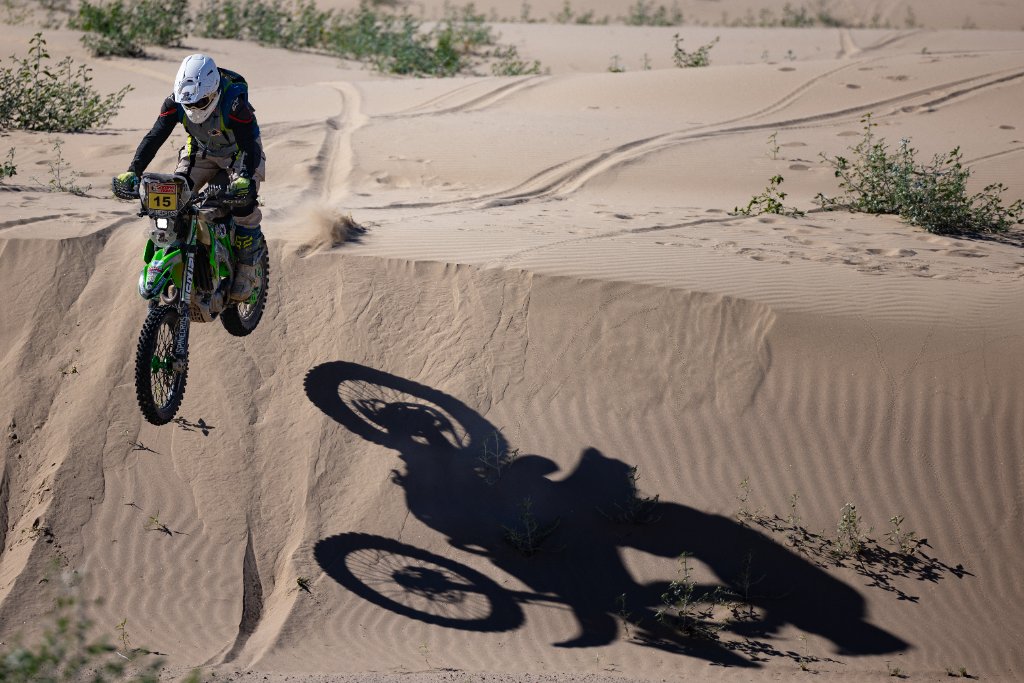 Off-road motorcycle rider frozen mid-air over a desert dune crest