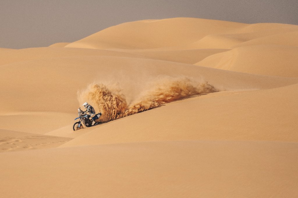 Off-road motorcycle racer carving through a steep sand dune