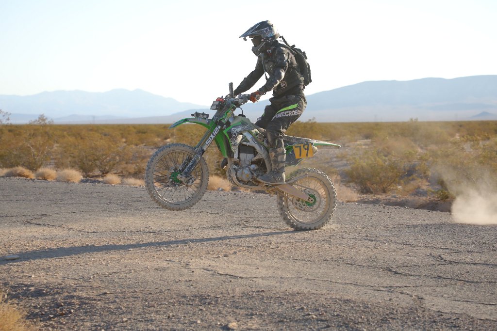 Off-road motorcycle rider performing a wheelie with SPINECROSS branding