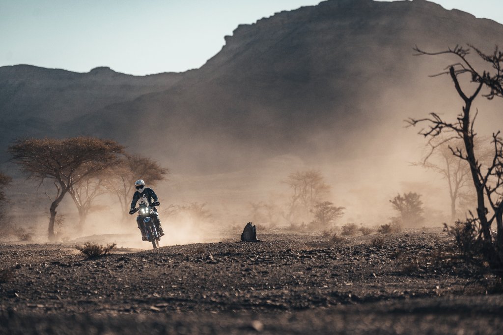 Off-road motorcycle rider crossing rocky desert terrain at golden hour