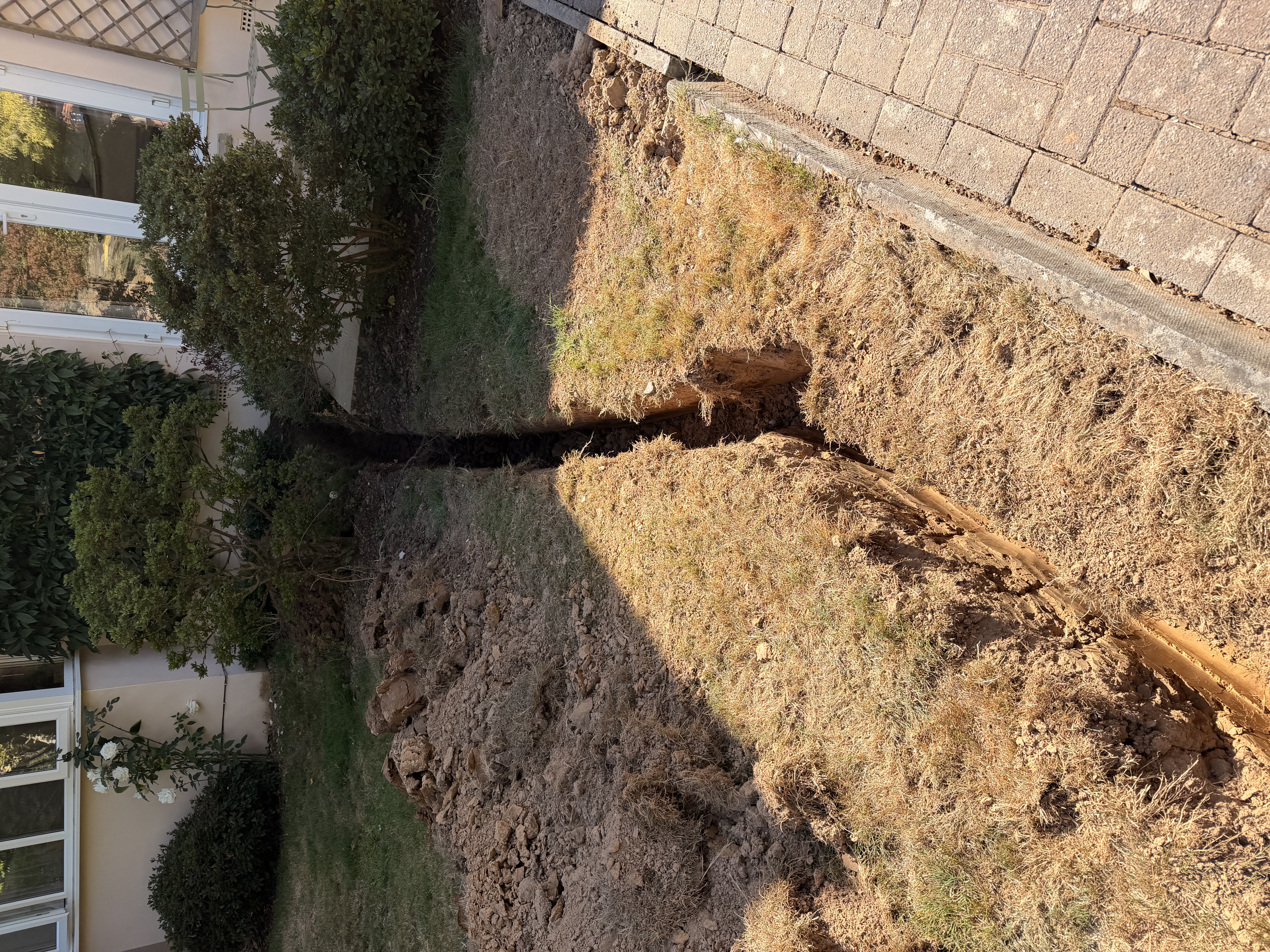 Freshly excavated narrow trench running alongside a garden path for drainage installation and utility trenching in Sussex by Subsoil Land & Water, drainage in Sussex and utility trenching contractors serving Kent and East Sussex