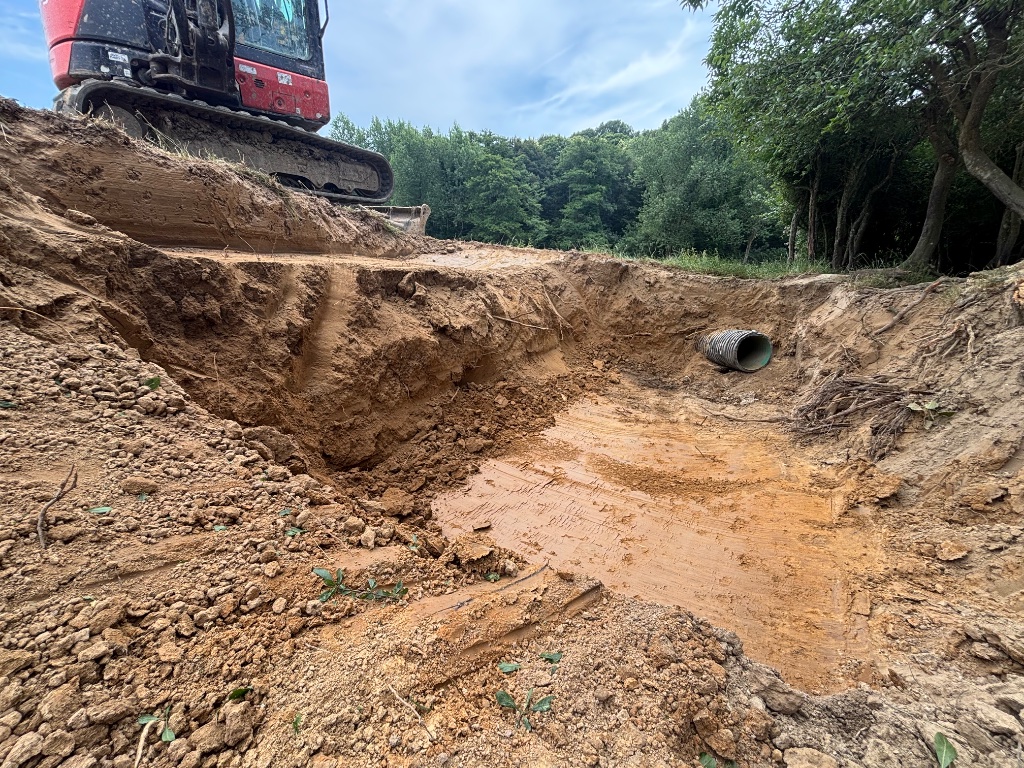 Deep trench earthworks and excavation with tracked excavator installing drainage pipe on a site clearance project in Battle, East Sussex by Subsoil Land & Water