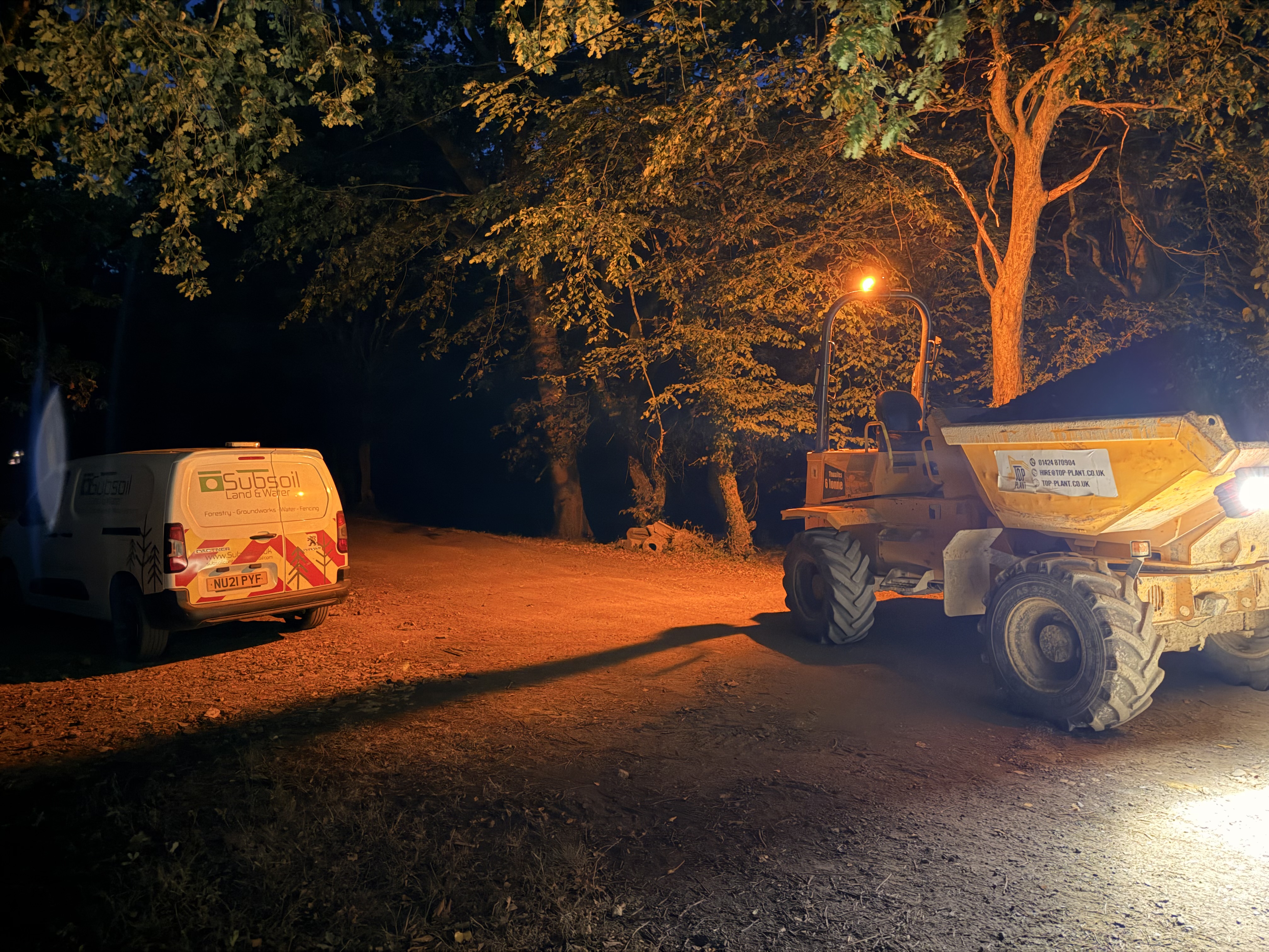 Night work road planings delivery on a farm track construction project near Battle, East Sussex — Subsoil Land & Water dumper truck delivering crushed concrete and road planings for access road sub-base preparation under floodlights in the East Sussex countryside