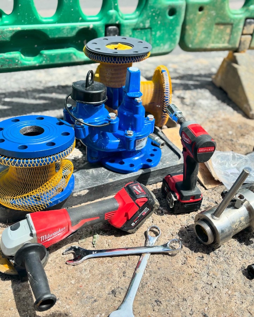 Professional water valve installation equipment including blue industrial valve, Milwaukee M18 cordless angle grinder and impact driver on construction site for water supply infrastructure by Subsoil Land & Water in Kent and East Sussex