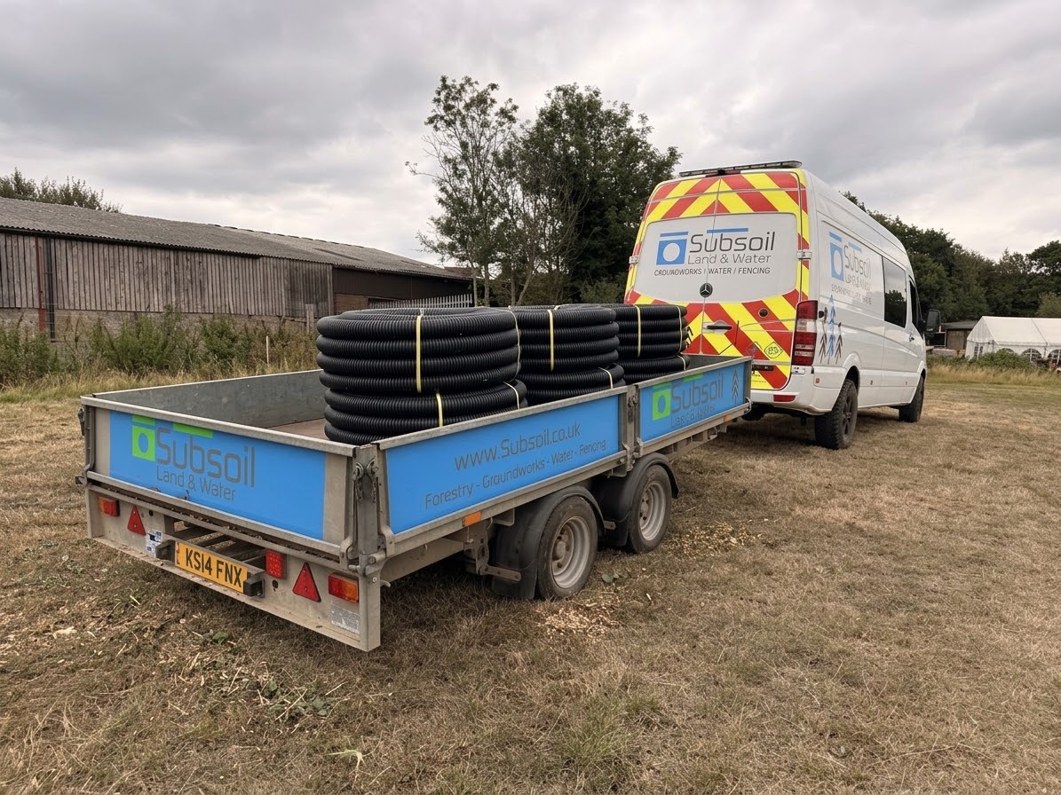 Subsoil Land & Water work van and trailer loaded with black corrugated land drainage pipes in a field near Battle, East Sussex — land drainage contractors serving Kent and the South East