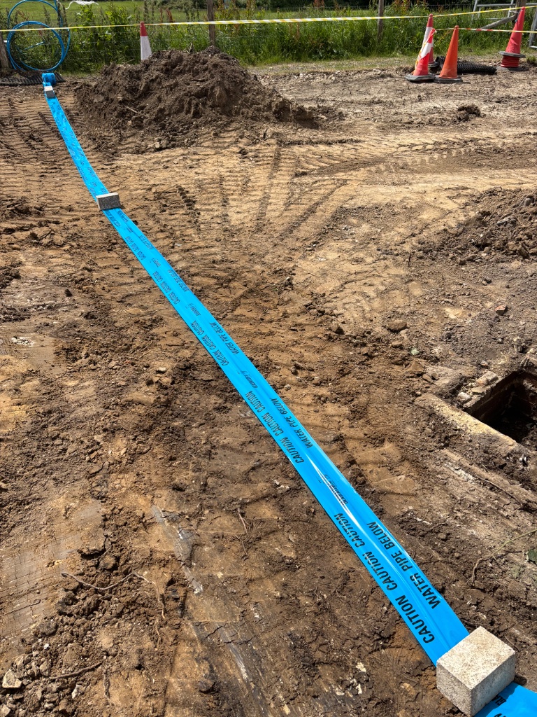 Professional water supply trenching and pipe installation by Subsoil Land & Water, showing blue caution water pipe below warning tape on groundworks site in Kent and East Sussex