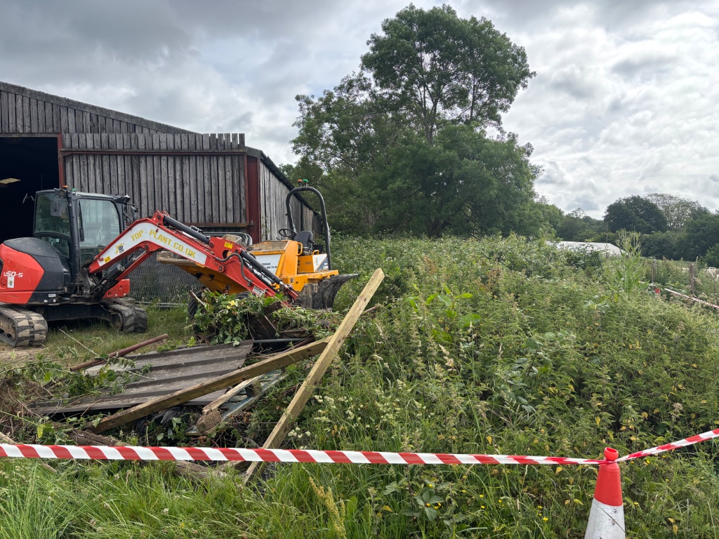 Kubota mini excavator clearing scrub and debris for groundworks and land development project at rural site with agricultural barn in Kent and East Sussex by Subsoil Land & Water
