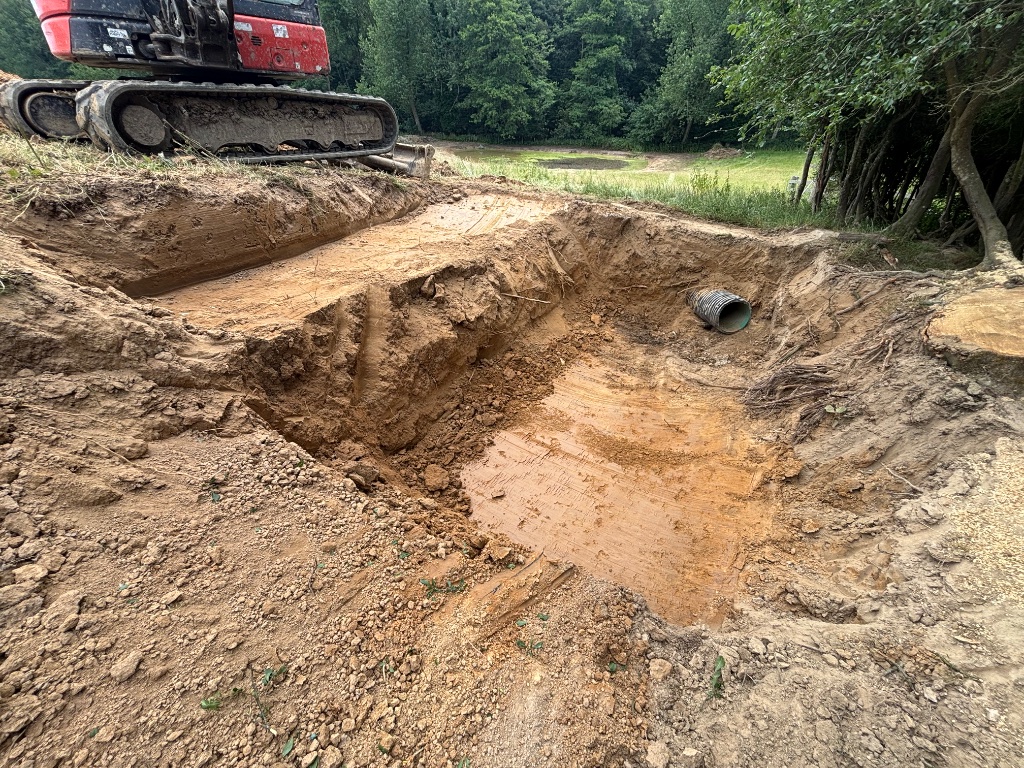 Deep stepped trench excavation for land drainage upgrades in Battle, East Sussex with tracked excavator installing corrugated drainage pipe by Subsoil Land & Water