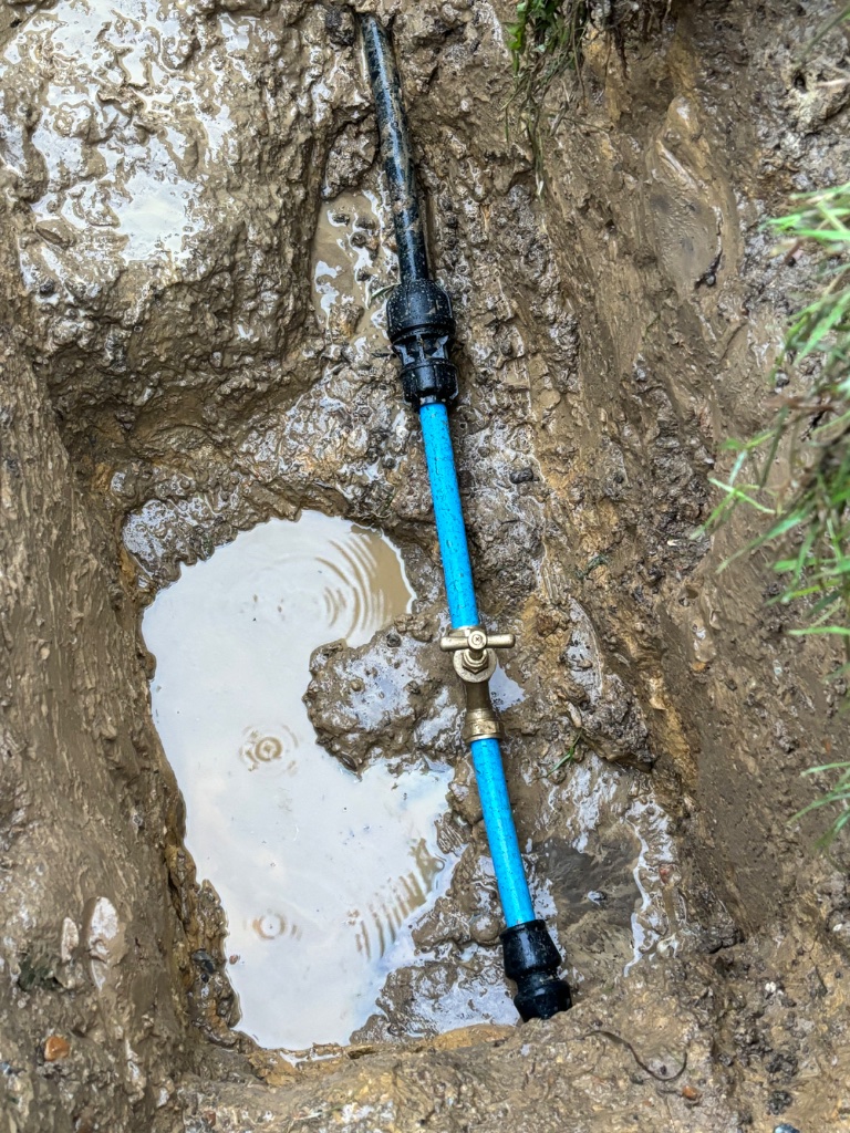 Water main repair showing blue HDPE pipe with brass service valve and compression couplings in trench by Subsoil Land & Water, water main repair contractors in Battle, East Sussex