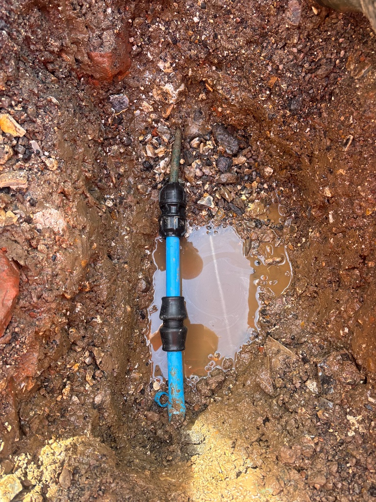 Water pipe repair with blue MDPE pipe and compression coupling fitting in excavated trench by Subsoil Land & Water, water pipe repair contractors serving the South East