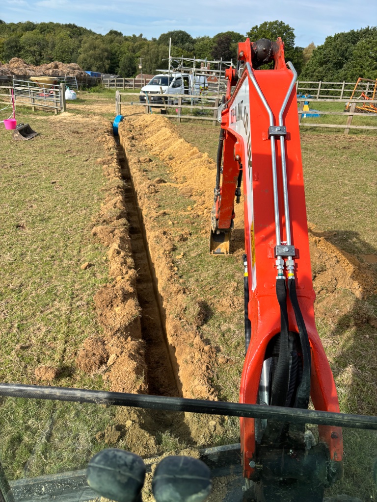 Excavator digging a deep trench for land drainage pipes during a professional groundworks project by Subsoil Land & Water in East Sussex