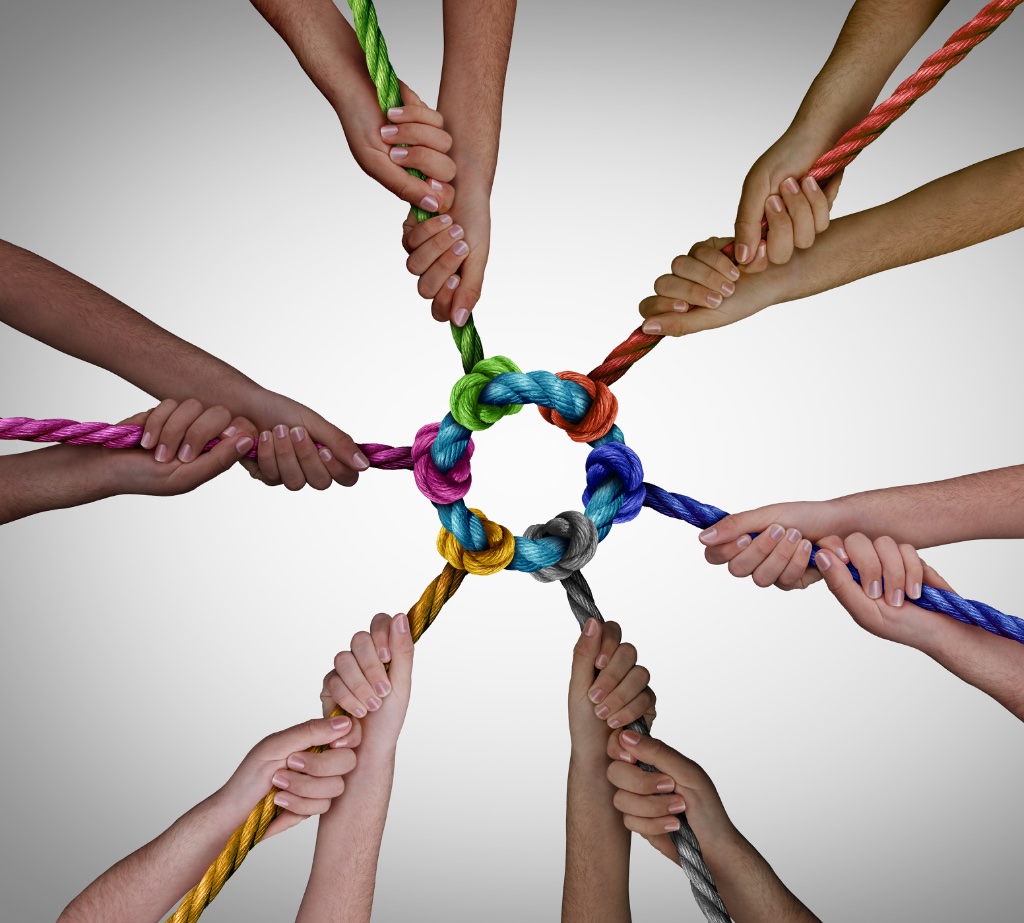 Eight hands holding multicolored ropes tied in a central knot