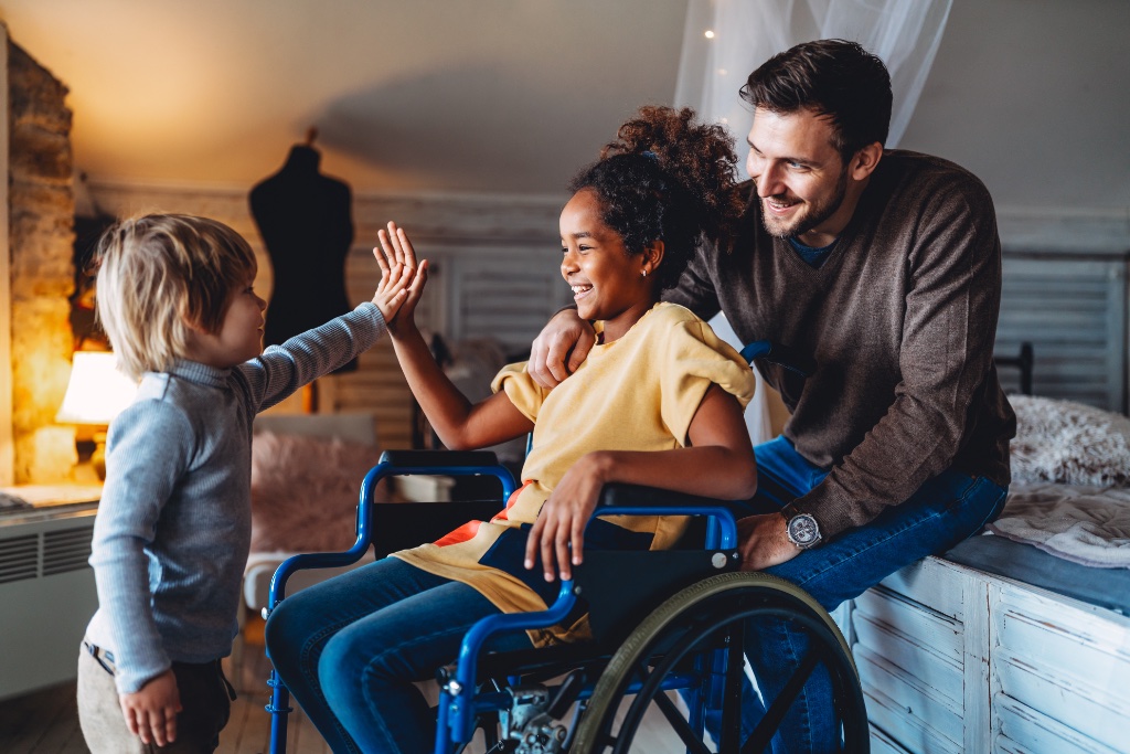 A caregiver supporting a child in a wheelchair, sharing a high-five — healthy social connectedness