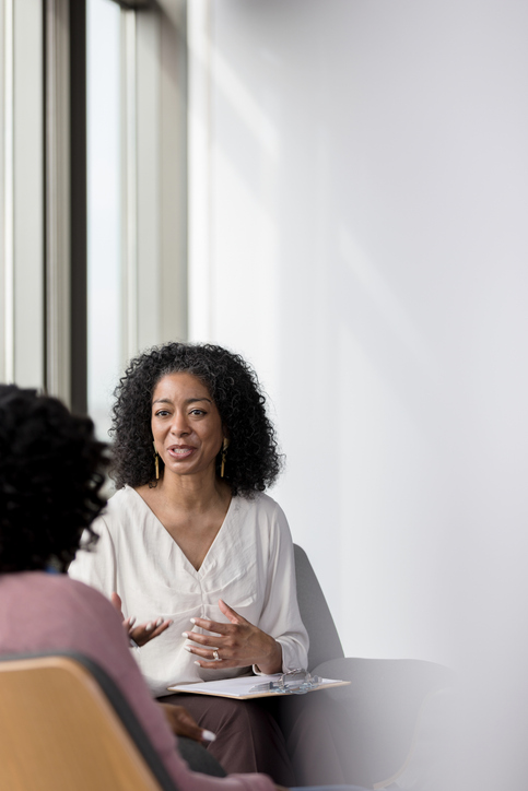A therapist in a light-filled room, speaking and listening with an open, empathetic gesture