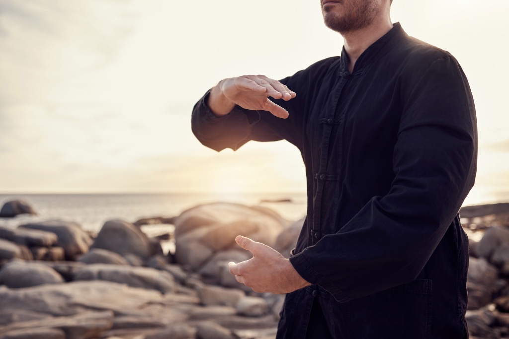 A person practicing Tai Chi on a rocky shoreline at golden hour