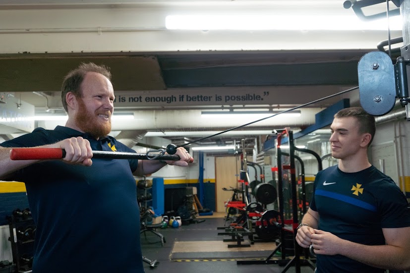 Coach guiding an athlete through a cable exercise in the gym