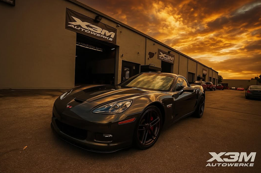 Dark Chevrolet Corvette at sunset in front of X3M Autowerke