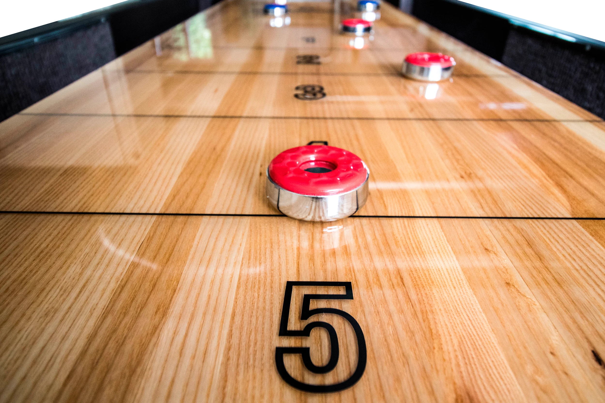 Close-up of a hand-finished shuffleboard playing surface with red and blue pucks