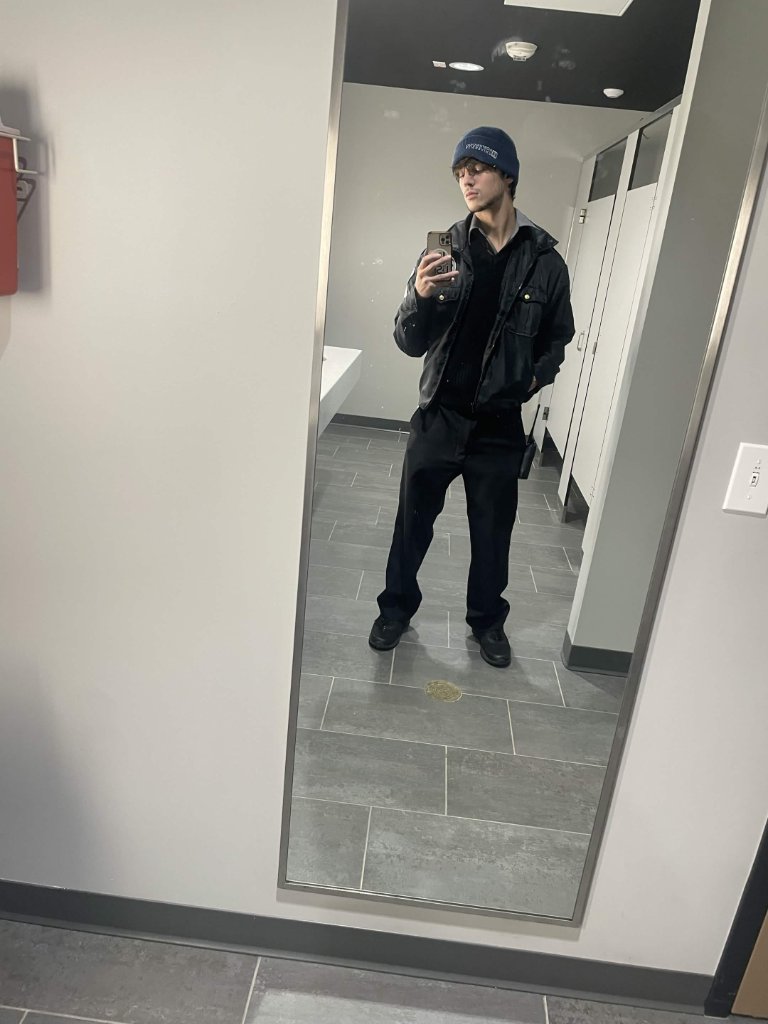 Portrait of Aiden Pierce in a black jacket and beanie taking a mirror selfie