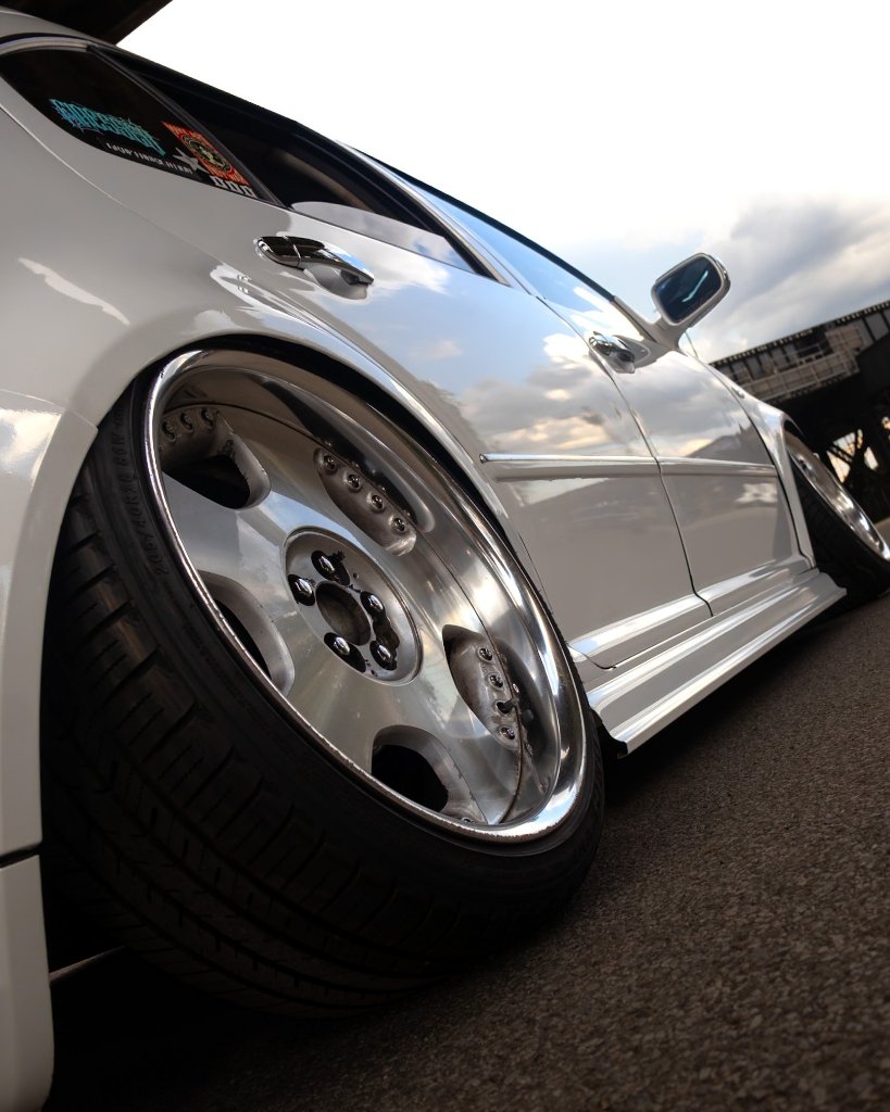 Low-angle close-up of chrome deep-dish wheel with extreme camber on white car
