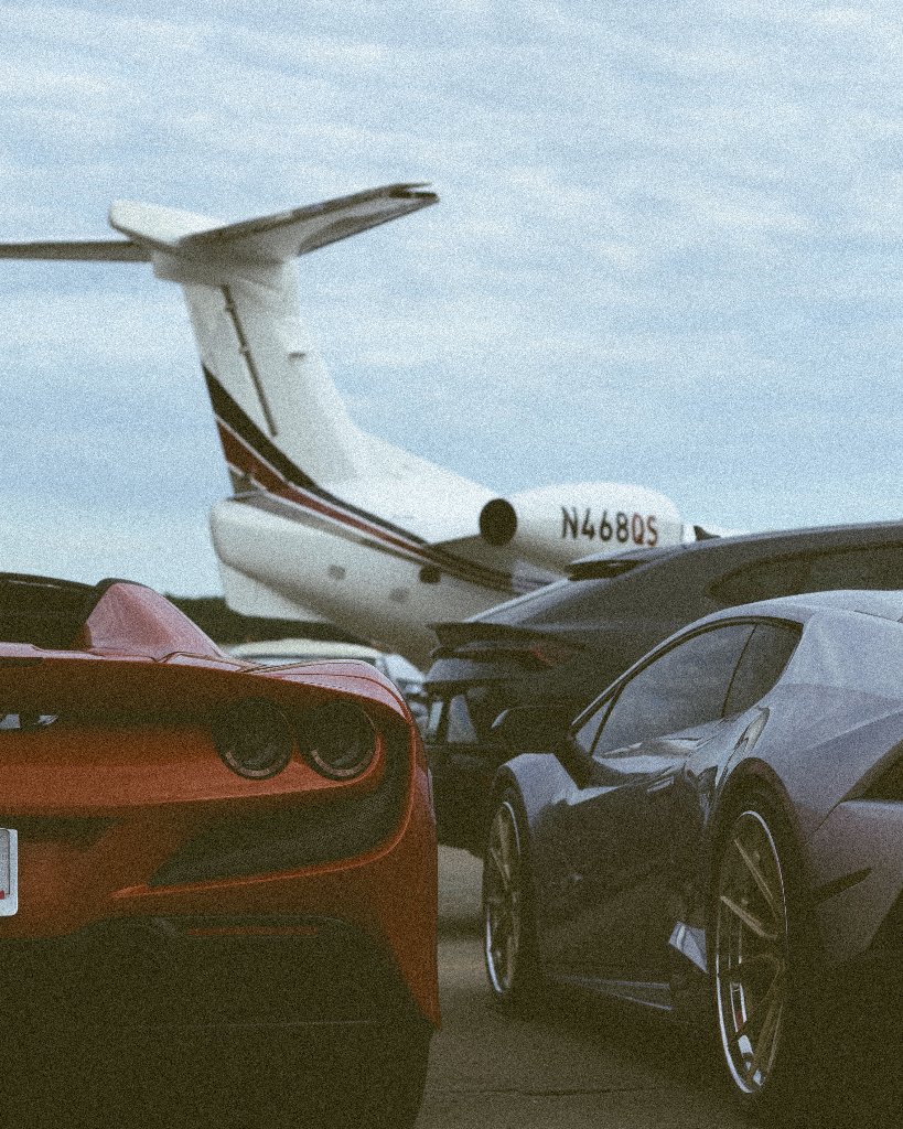 Orange and grey sports cars parked on tarmac with private jet in background