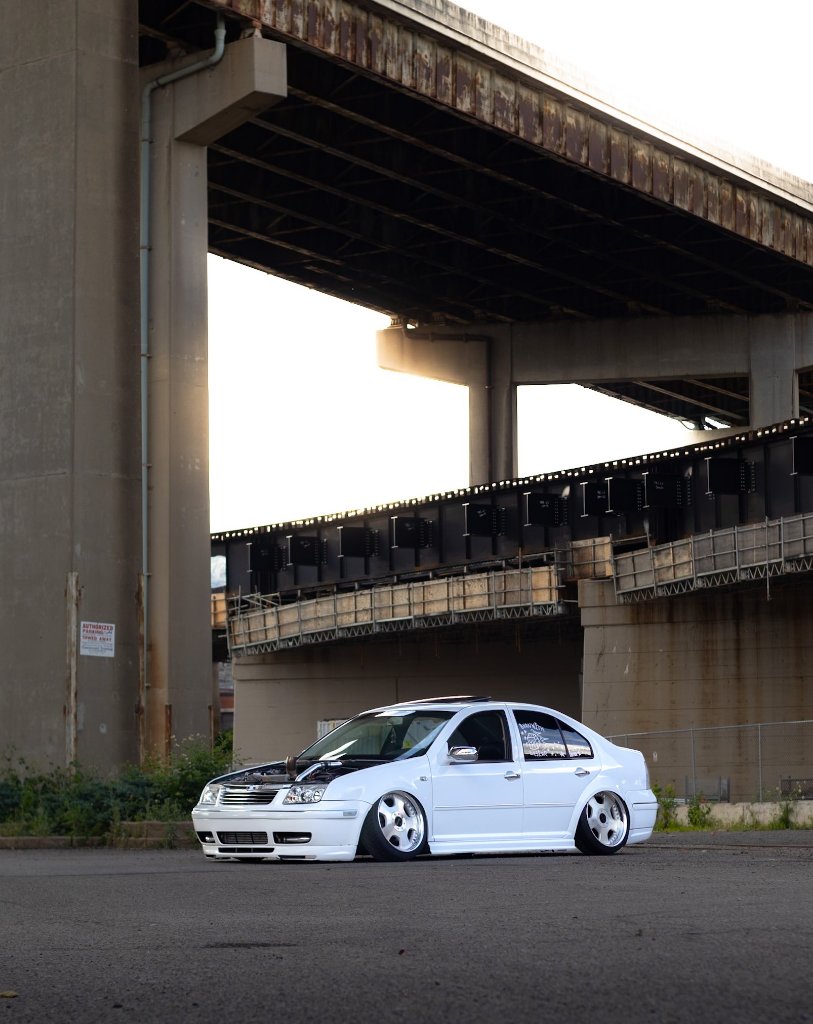 White Volkswagen Jetta with wide body kit under highway overpass at golden hour